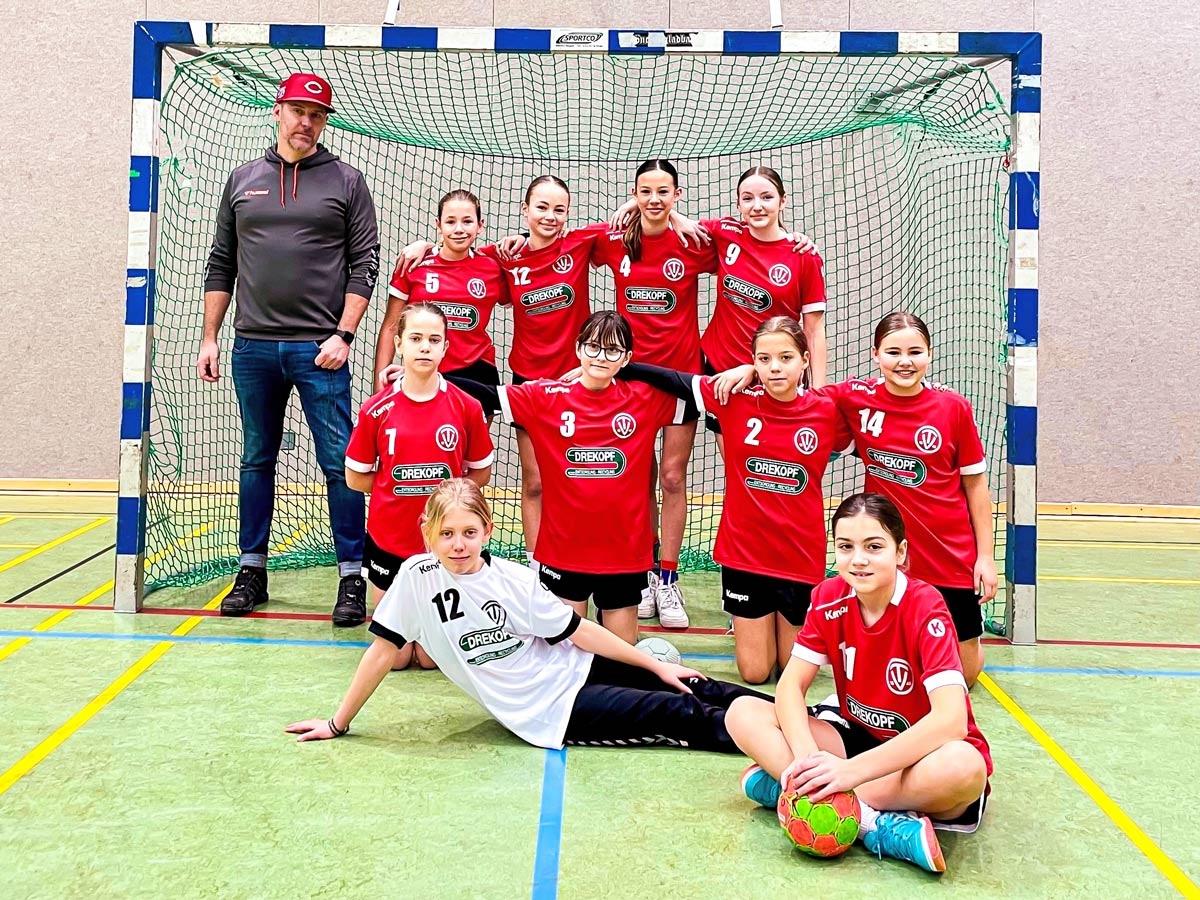 Handballteam Mädchen sitzt und steht mit Trainer im Tor