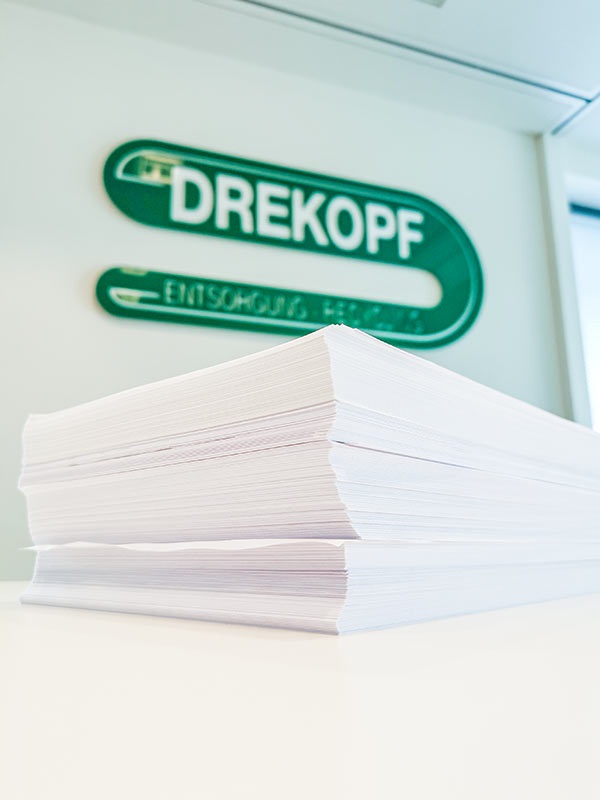 Papierstapel vor Drekopf Logo
